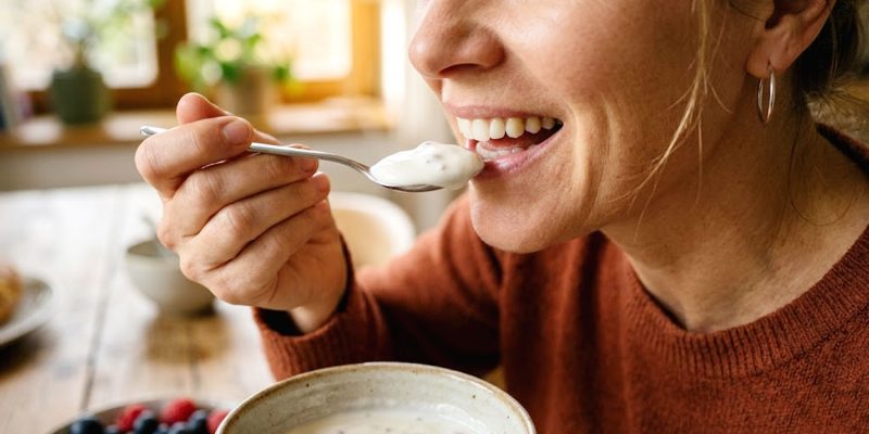 Eine Frau nimmt einen Löffel probiotischen Joghurt zu sich – Symbolbild für ein gesundes Mund- und Darmmikrobiom.